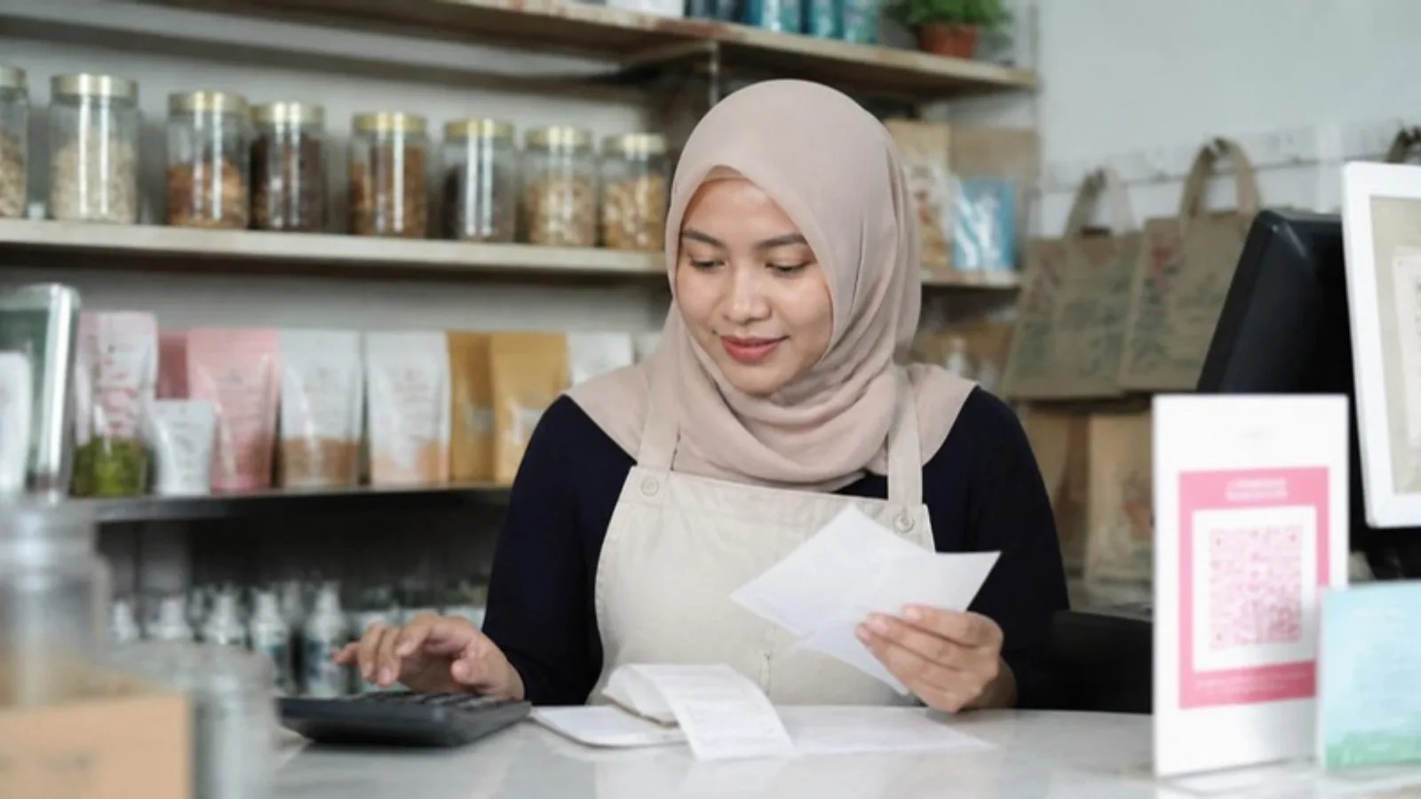 A confident small business owner reviewing invoices and receipts at the counter of their shop