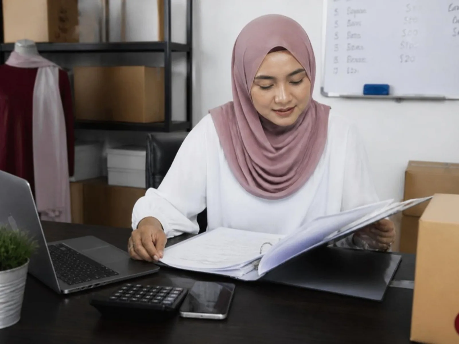 Seorang pemilik perniagaan menyemak rekod pelanggan dalam fail binder di sebuah meja